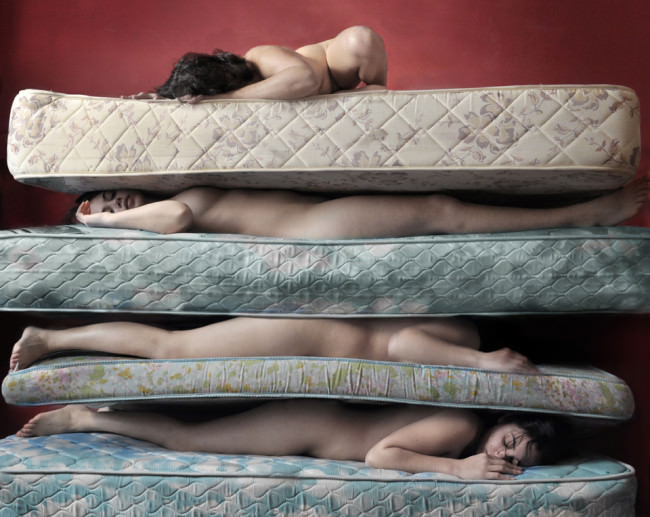 Nackte Menschen liegen gestapelt unter Matratzen.