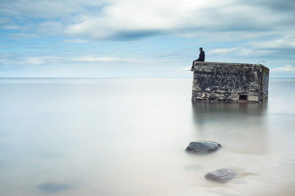 Eine Person sitzt auf dem Rand eines Bunkers, der aus der Meeresoberfläche ragt.