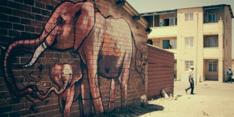 Ein Mann überquert eine Straße, neben ihm ein Wandbild mit Elefanten auf einer Backsteinmauer.