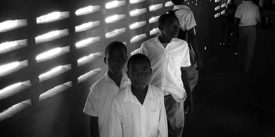 Mehrere Jungen in Schuluniformen vor einer Wand, durch die Licht durch Löcher fällt.