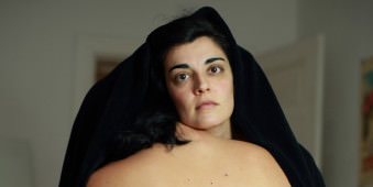 Eine Frau schaut unter einem schwarzen Tuch hevor.