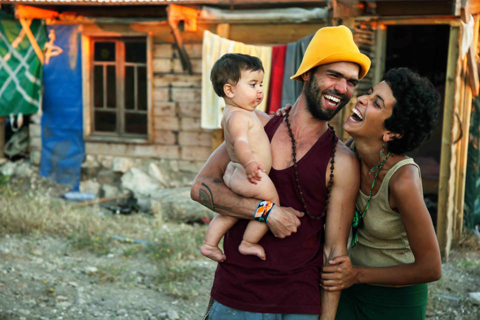 Eine dreiköpfige Familie steht lachend vor einem Haus