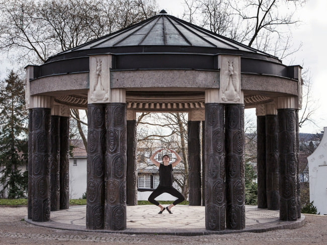Eine Tänzerin in schwarzem Anzug springt unter einem Pavillon.