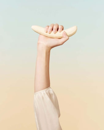 Eine Frauenhand hält eine geschälte Banane nach oben