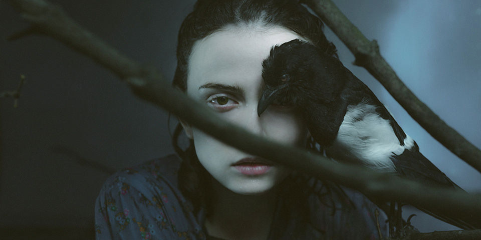 Ein bleiches Mädchen hält einen Vogel vor ihr Gesicht.