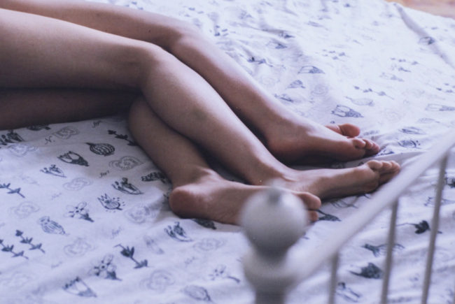 Die Beine eines Paares liegen auf einem Bett.