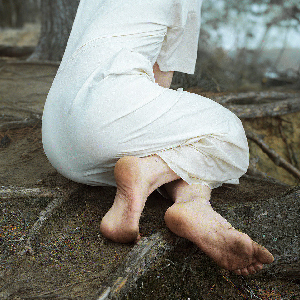 Eine Frau mit nackten Füßen und weißem Kleid sitzt auf dem dreckigen Boden.