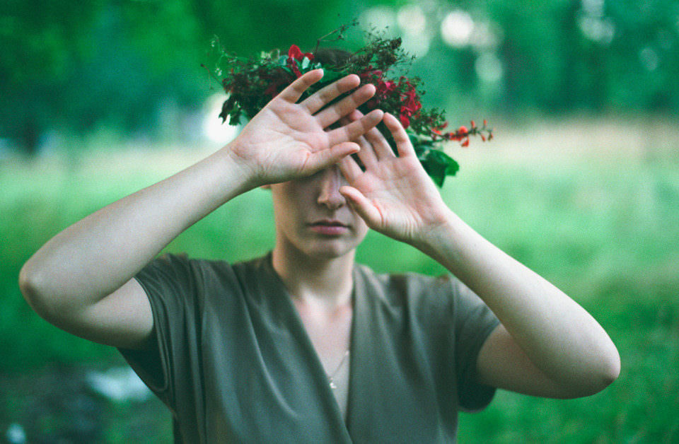 Eine Frau mit Blumenkranz im Haare hält sich die Augen zu.