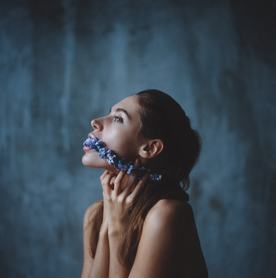 Eine Frau hat einen blaue Blumengirlande im Mund.