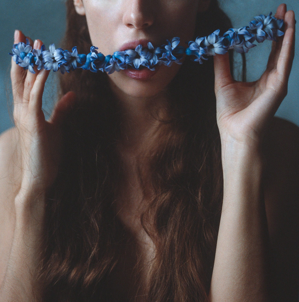 Eine Frau hat einen blaue Blumengirlande im Mund.