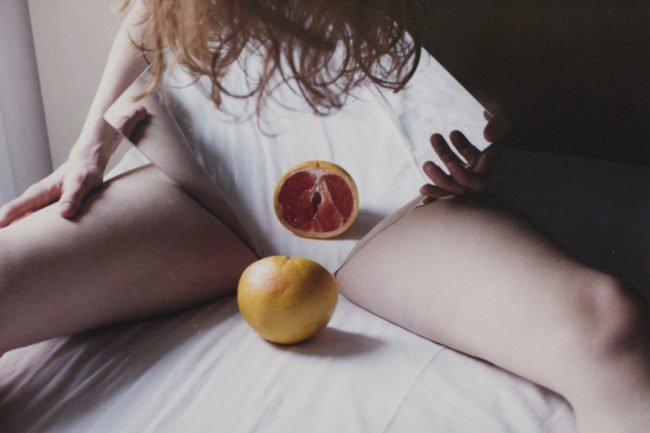 Eine Frau fält einen Spiegel und eine Orange zwischen ihren Beinen.