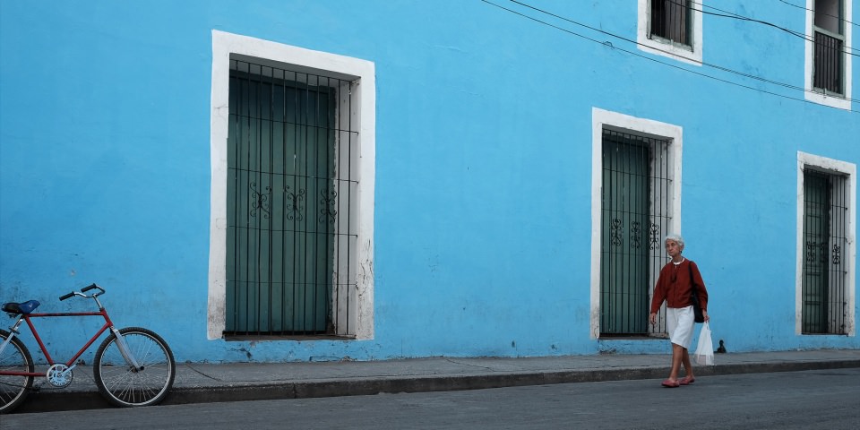 Eine Frau geht vor einer blauen Hausfassade entlang, an der auch ein Fahrrad lehnt.