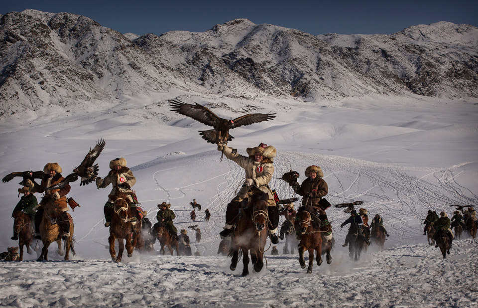Eine Gruppe Personen reitet mit Adlern durch den Schnee