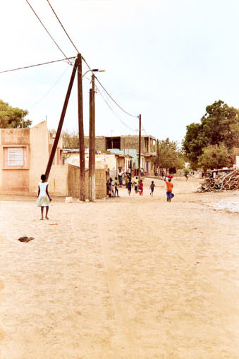 Menschen in der Ferne auf einer Sandstraße mit Telegrafenmasten.