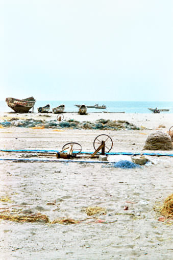 Strandblick mit Horizont an dem Boote liegen und Fischernetzspulen aufgebaut sind.