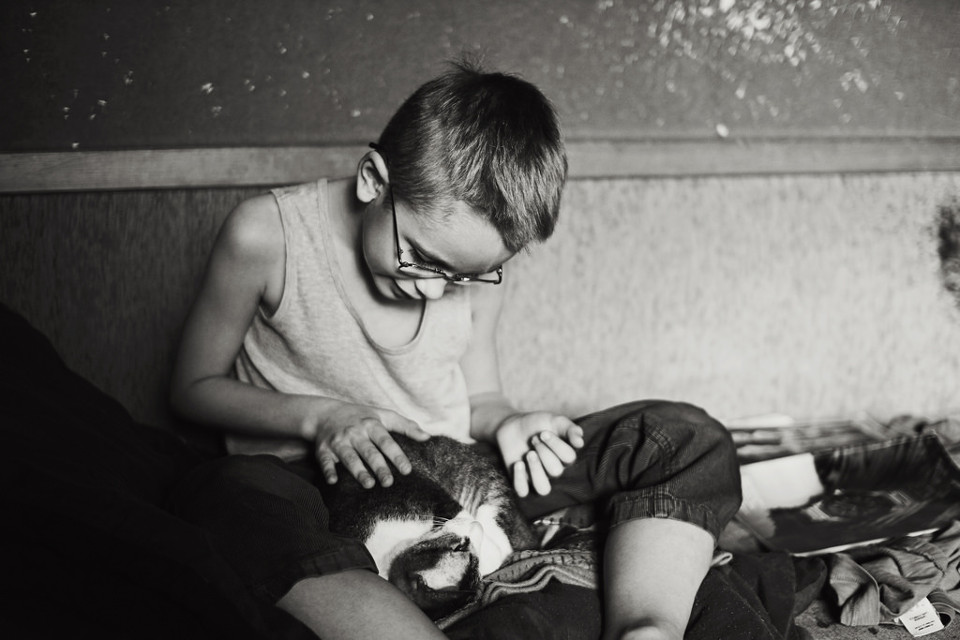 Schwarzweißfoto eines Jungen, wie er mit einer Katze spielt.