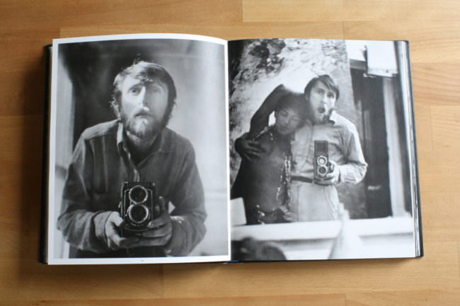 Schwarzweißfoto von einem Mann mit Kamera in einem Buch.