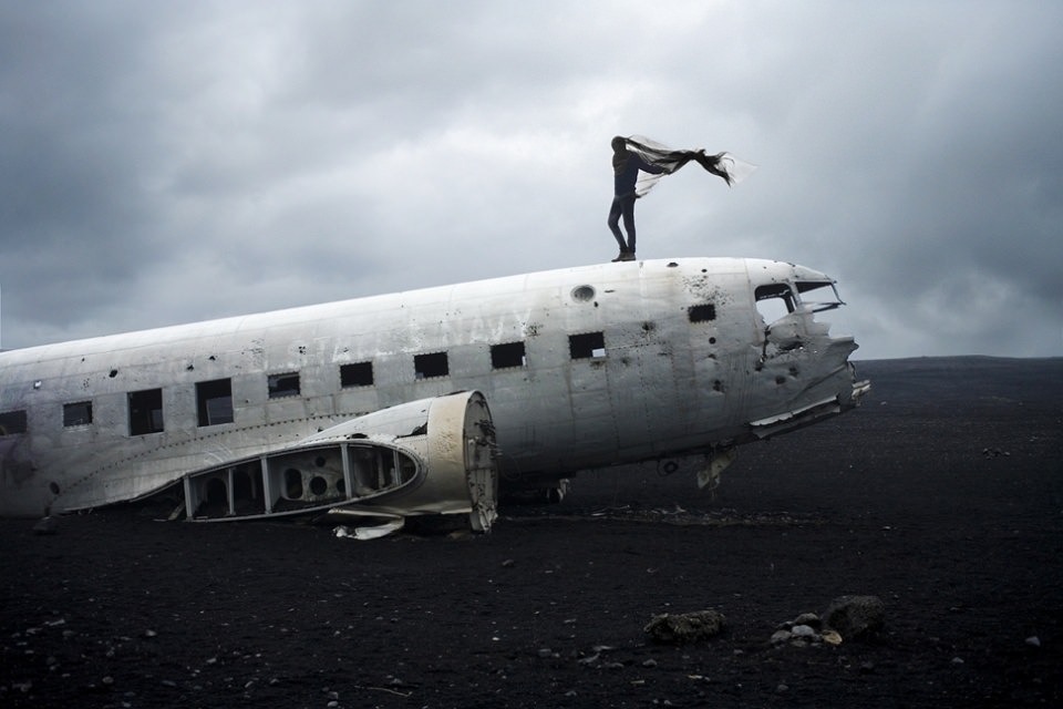 Ein Mensch mit wehendem Umhang steht auf einem Flugzeugwrack.