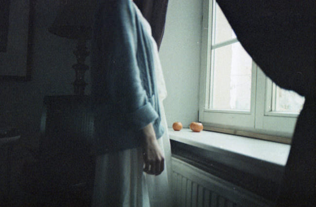 Eine Frau steht am Fenster, auf dem Fensterbrett liegen Orangen.