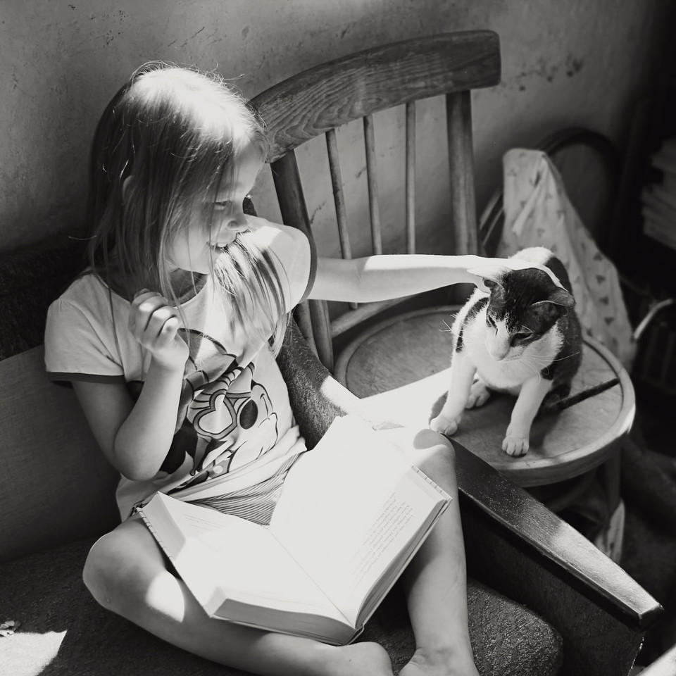 Schwarzweißfoto eines Mädchens beim Lesen mit einer Katze.