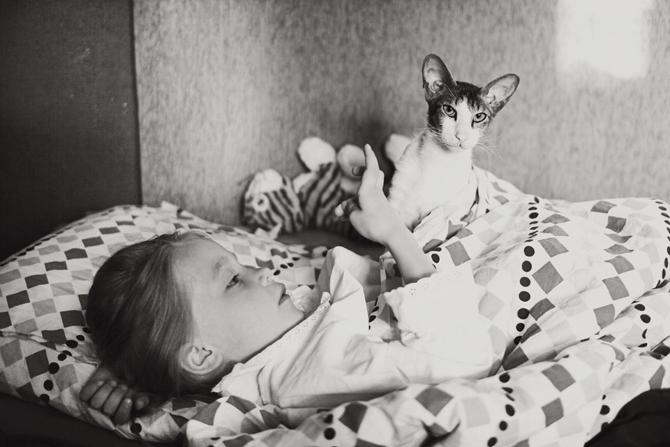Schwarzweißfoto eines Mädchens im Bett mit einer Katze.