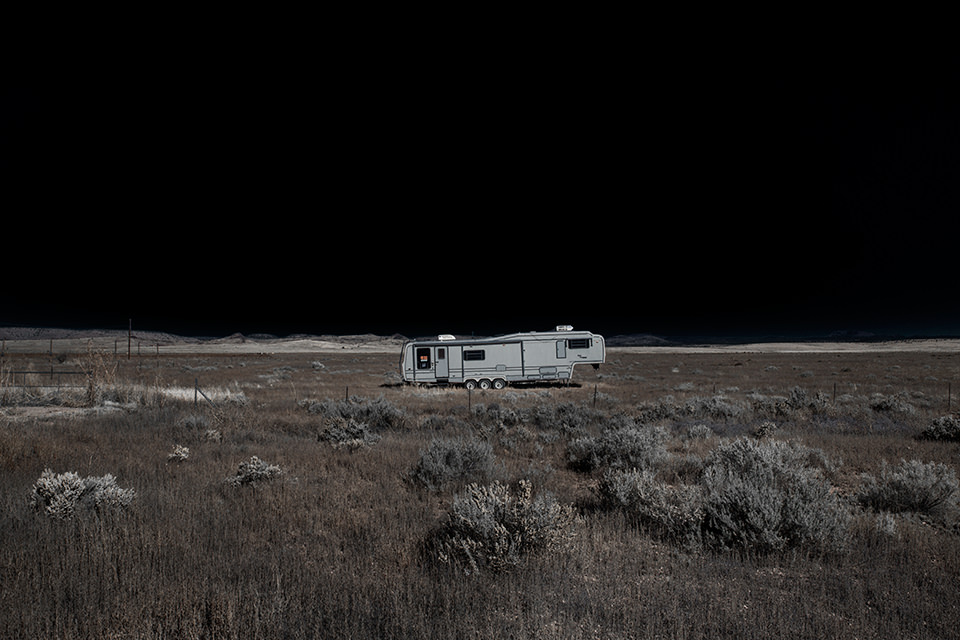 Eine ausgeleuchtete Wüstenlandschaft mit einem alten Camper vor Nachthimmel.
