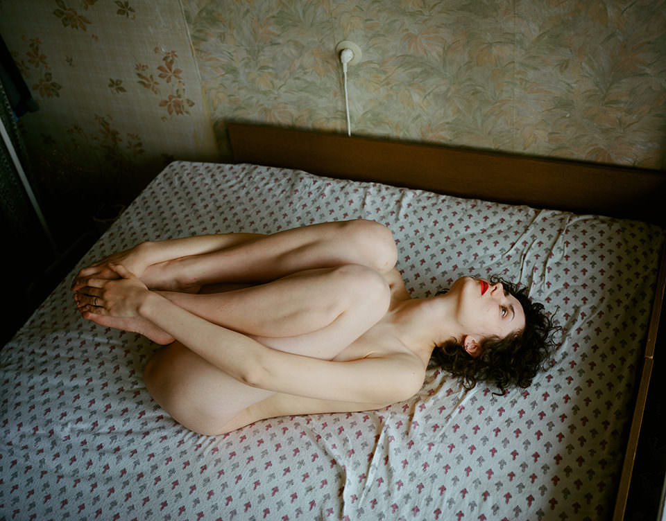 Eine unbekleidete Frau liegt auf dem Bett und schaut mit angezogenen Beinen zur Decke