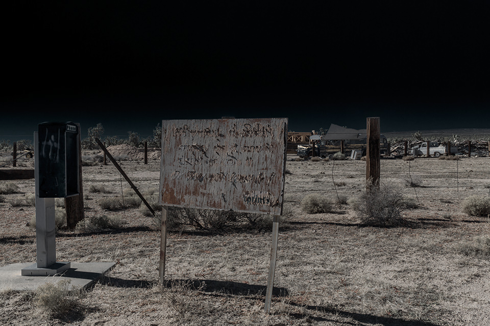 Eine ausgeleuchtete Wüstenlandschaft mit einem alten Schild und Stacheldrahtzaun.