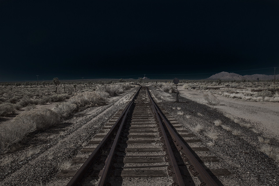 Eine ausgeleuchtete Wüstenlandschaft mit Gleisen, die zum Horizont führen.