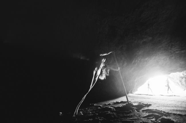 Eine Frau in einer Höhle, davor vorbeigehende Menschen.
