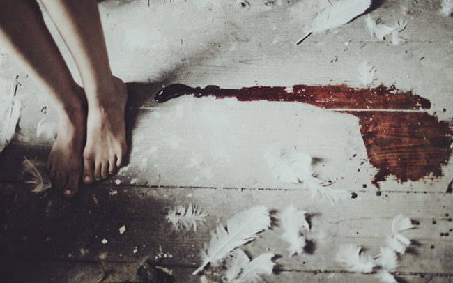 Nackte Füße, weiße Federn und eine Blutspur ergießt sich über den Holzboden.