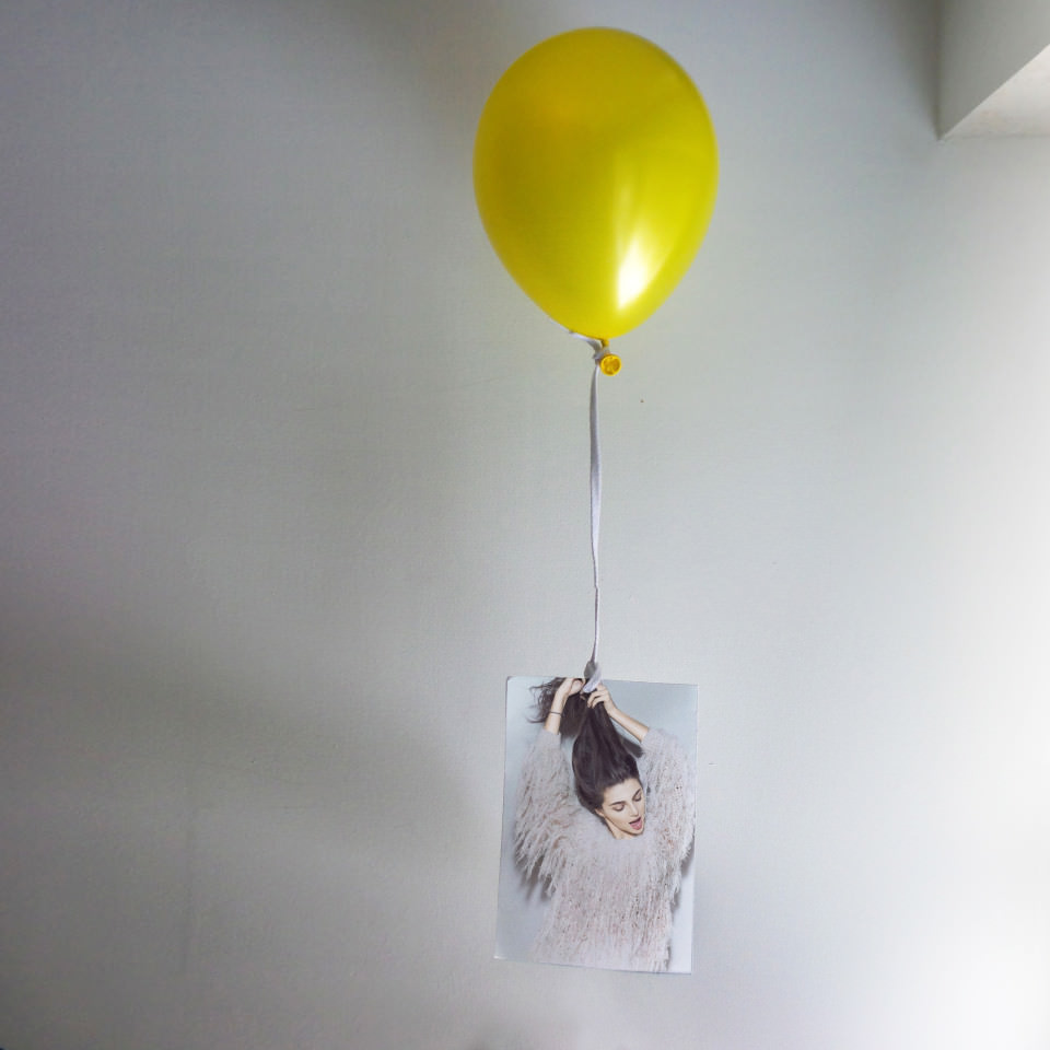 Ein gelber Luftballon hängt an einem Foto einer Frau.