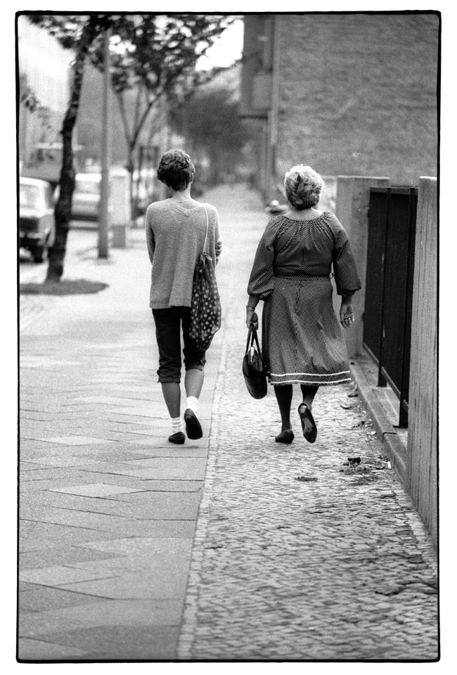 Zwei Personen gehen eine Straße entlang, man sieht ihren Rücken.