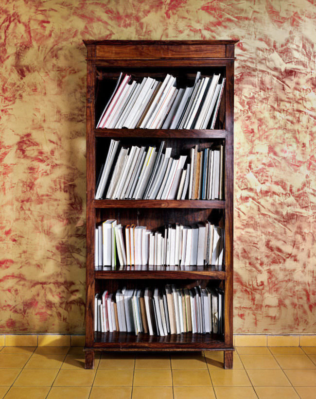Ein volles Bücherregal, bei dem man aber nur die Rückseiten der Einbände sieht.