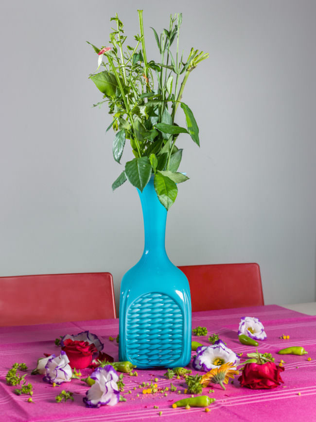 Ein Strauß Blumen steht in einer Vase, alle Blumenköpfe liegen daneben auf dem Tisch.
