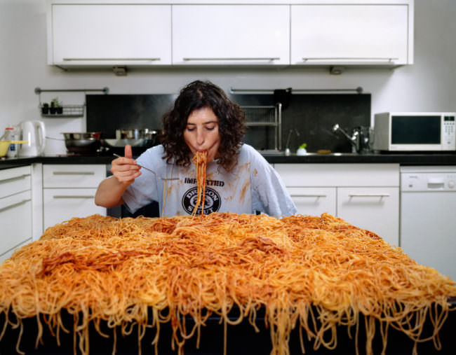 Eine Frau isst eine riesige Portion Spaghetti direkt vom Tisch.