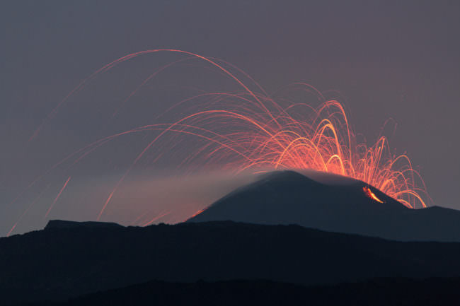 Rote Funken eines Vulkans über eines nächtlichen Landschaft.