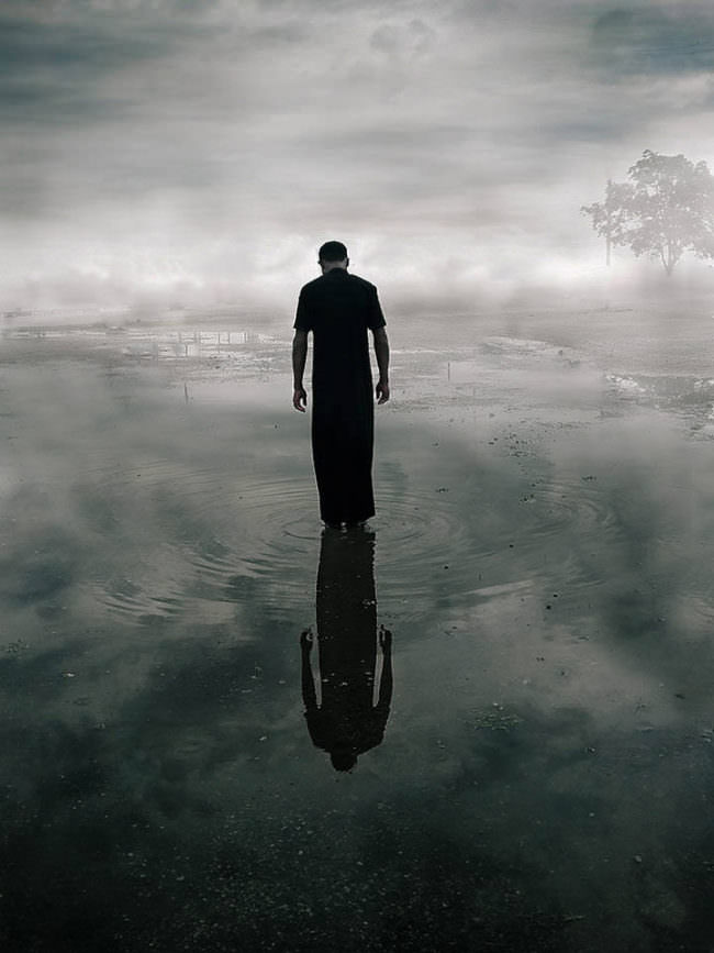 Eine Person steht im Wasser, Wolken spiegeln sich darin.