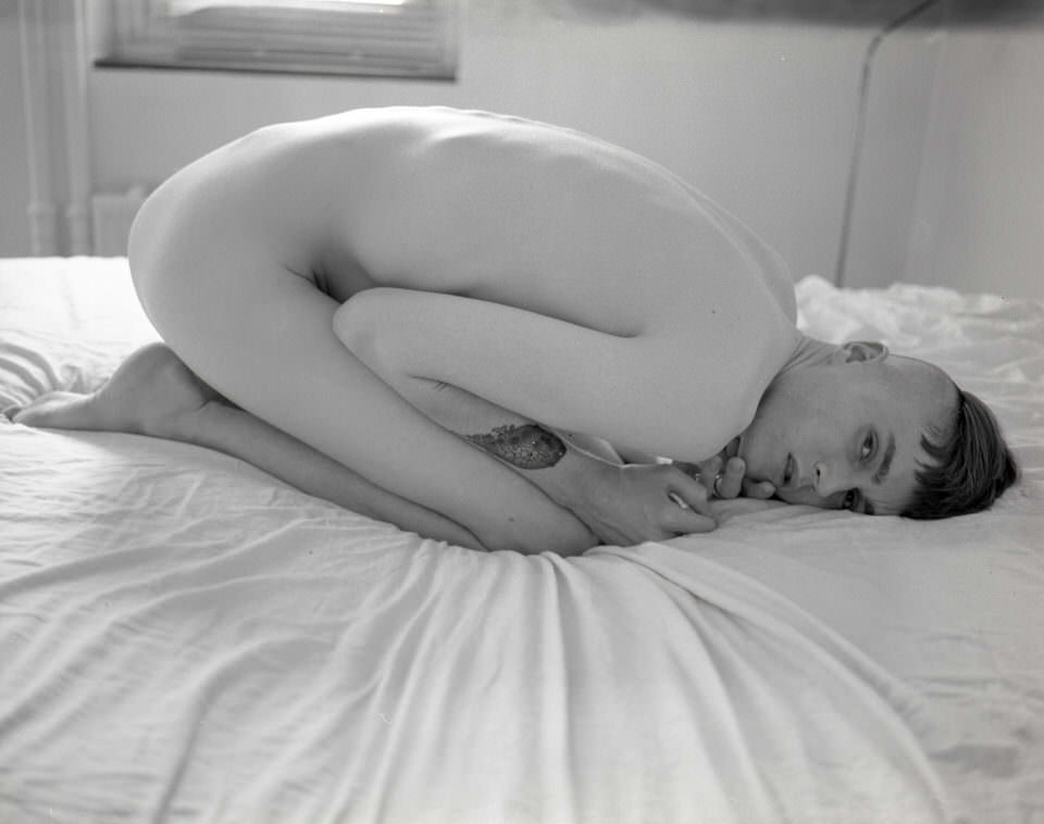 Ein Mann in Embryopose auf einem Bett