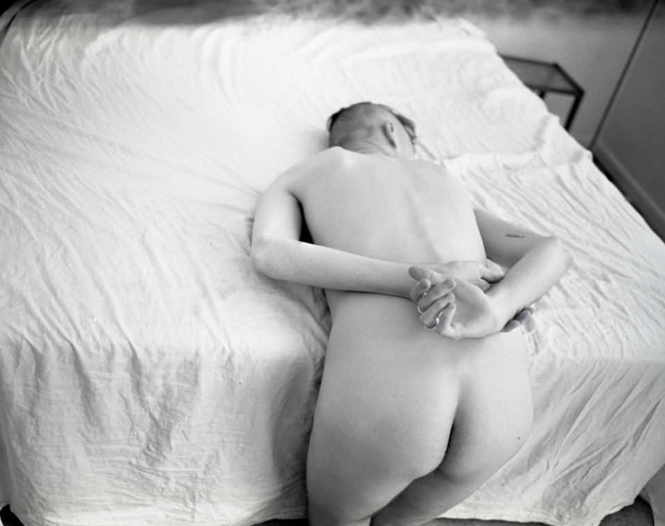 Ein Mann nackt vornübergebeugt auf einem Bett