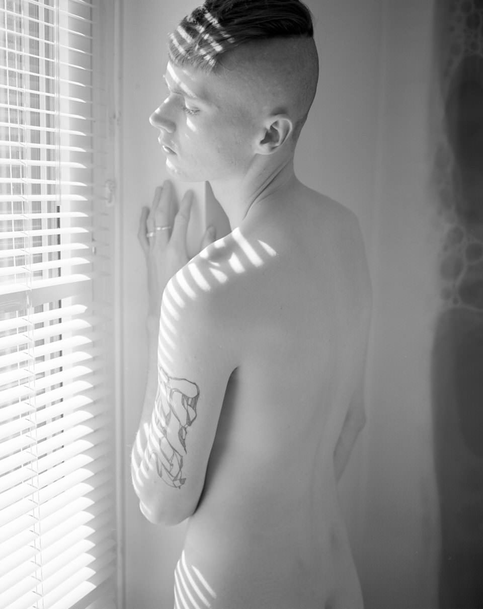 Ein Mann posiert nackt vor einem Fenster