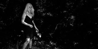Frau in kurzem schwarzen Kleid vor dunklem Waldhintergrund.