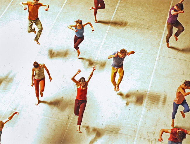 Tanzende und springende Personen in bunten Kleidungsstücken von oben dargestellt.
