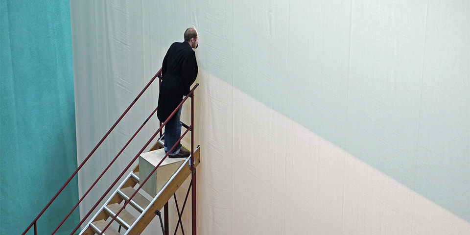 Mann steht auf Treppe und schaut durch ein Loch in einer Wand.