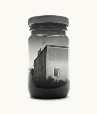 Abbildung eines Marmeladeglases vor hellem Hintergrund, auf dem eine Hausecke zu sehen ist.