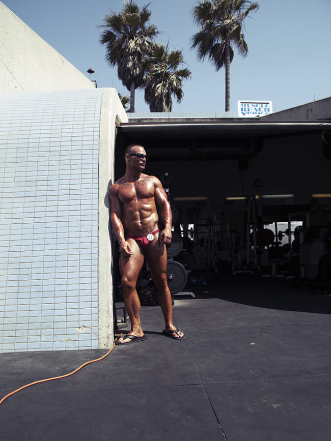 Muskulöser Mann steht im Kontrast an einer Mauerecke.