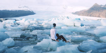 Ein Mann sitzt inmitten einer Eislandschaft und hat ein kaputtes Fischglas auf dem Kopf.