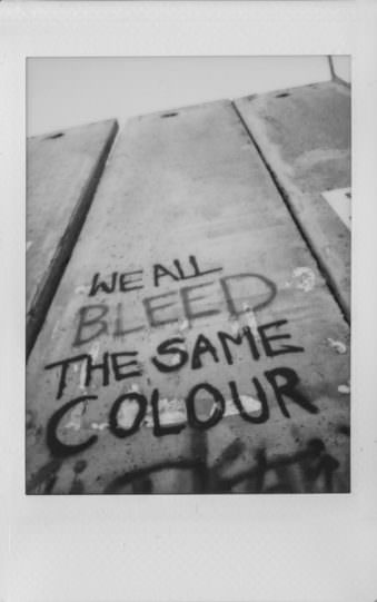 Auf einer Mauer steht „We all bleed the same colour"