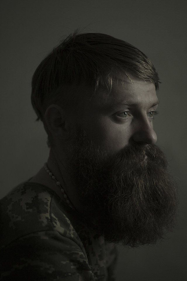 Portrait eines jungen Mannes in Flecktarn mit langem Bart. Die Lichtstimmung ist recht düster gehalten.