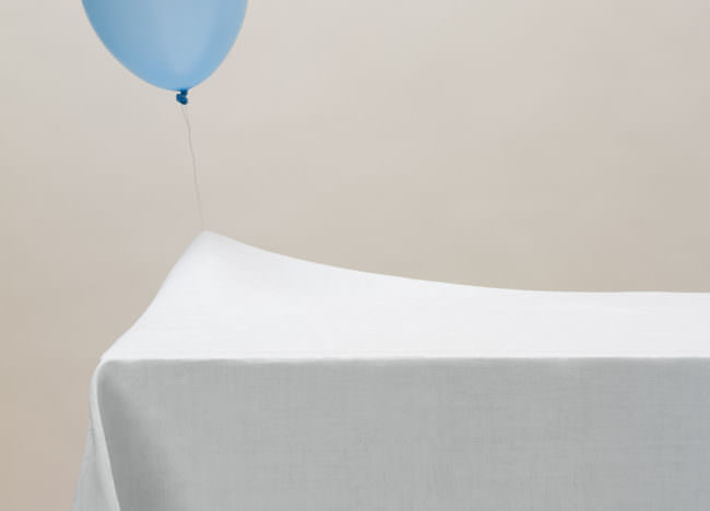 Ein blauer Luftballon an einer Schnur strebt nach oben und hängt jedoch unten an einer weißen Decke fest.